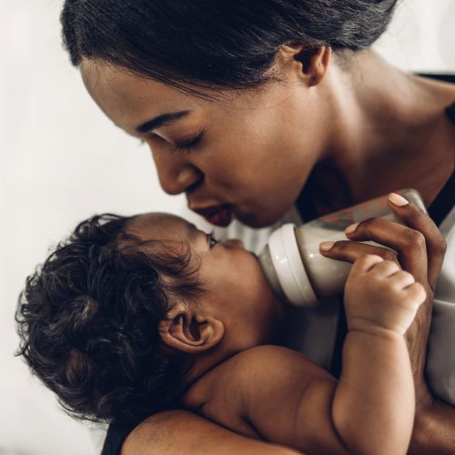 Portrait of enjoy happy love family african american mother play Portrait of enjoy happy love family african american mother playing with adorable little african american baby.Mom feeding bottle of milk to baby cute son in a white bedroom.Love of black family concept